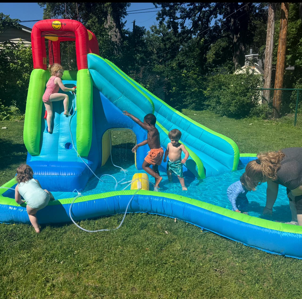 Children playing on a blue and green inflatable water slide in a backyard