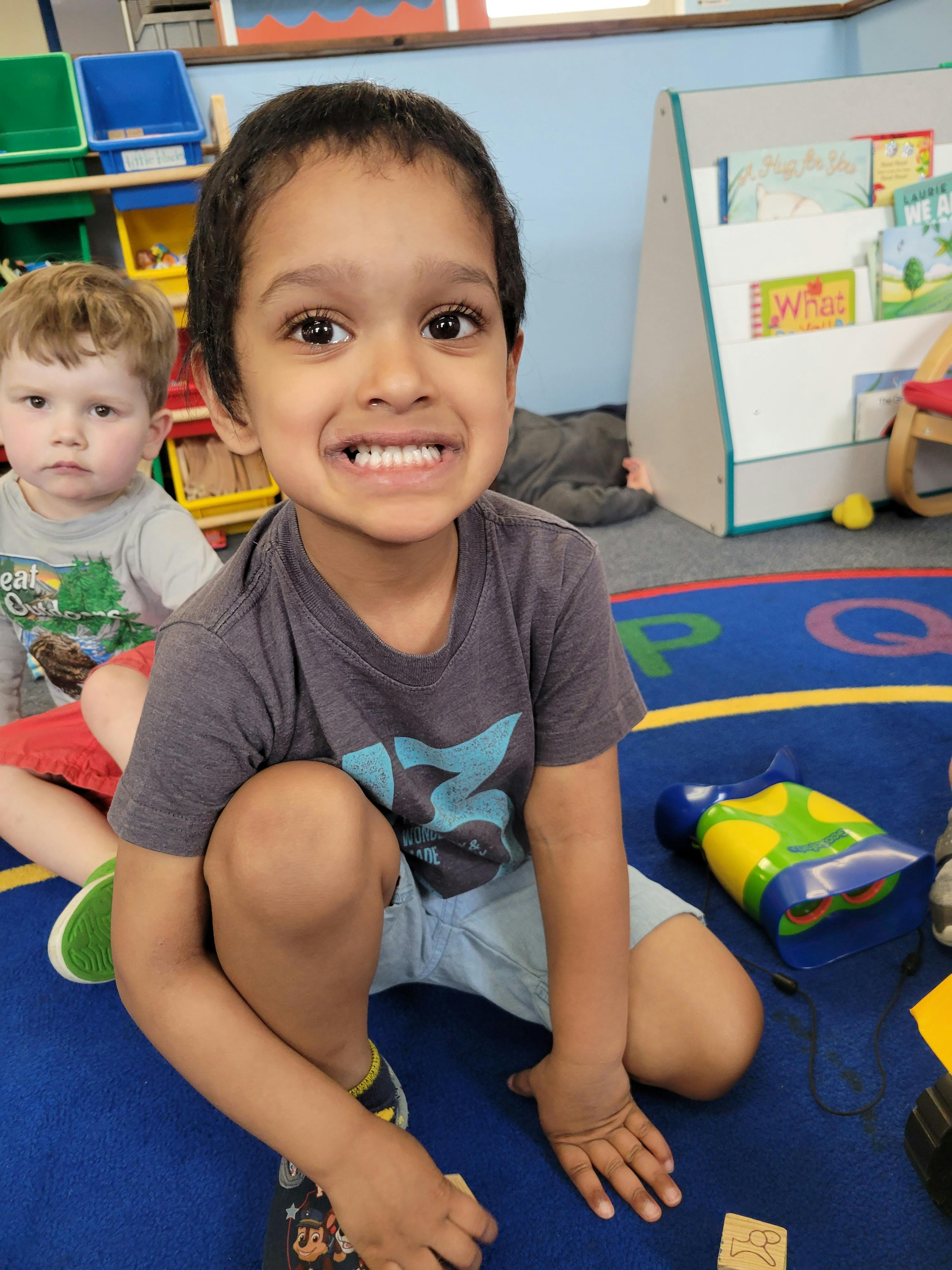 Child smiling at camera, another child in background in a classroom
