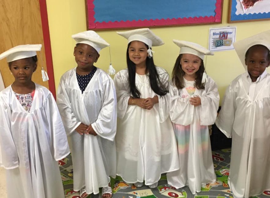 Five children in white graduation caps and gowns