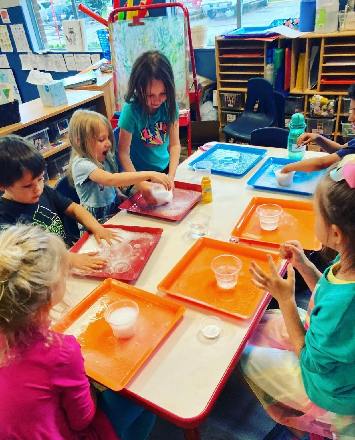 Children at a table engaged in a classroom activity with trays and cups