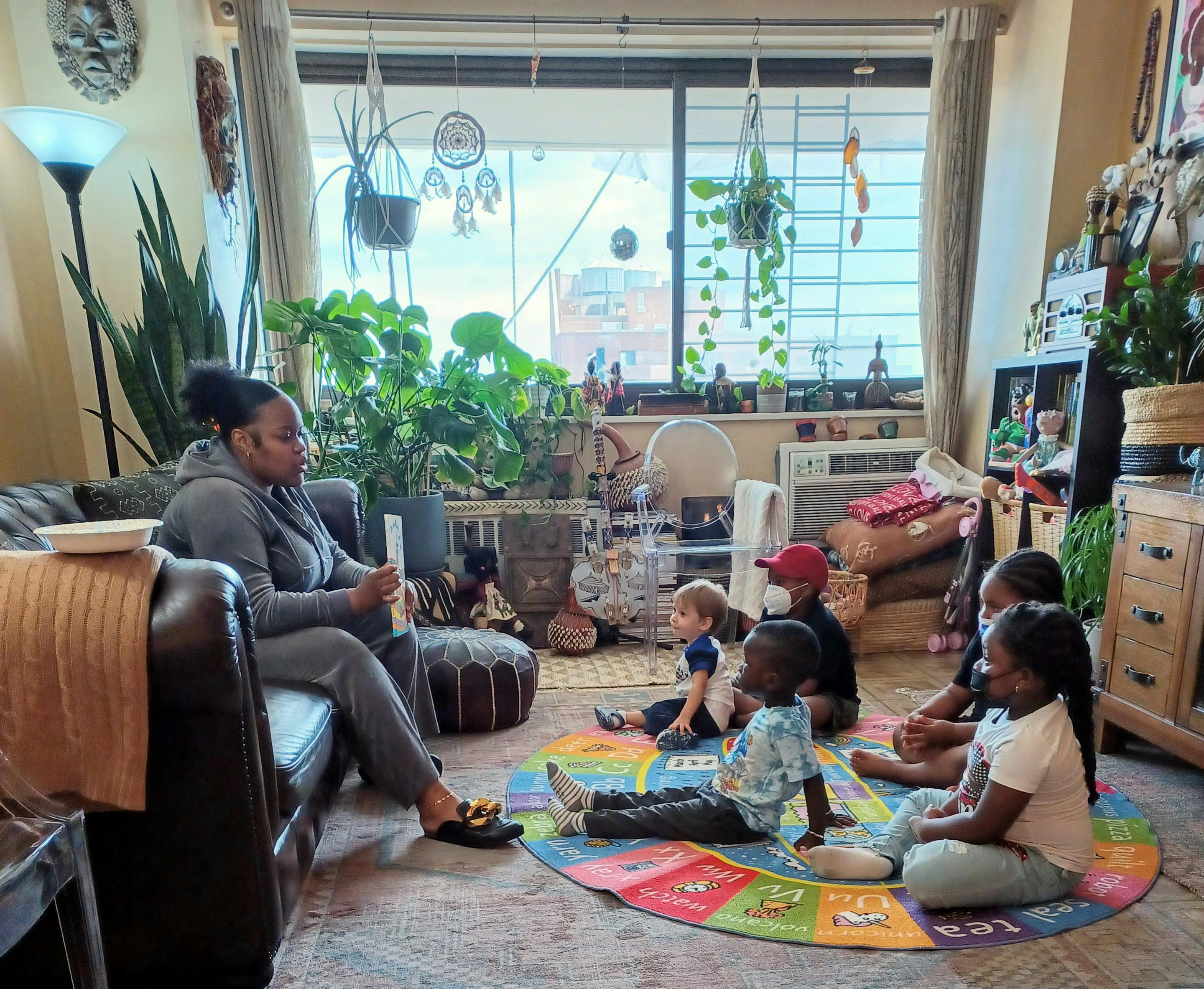 Adult sitting on a couch reading a book to a group of children on a rug