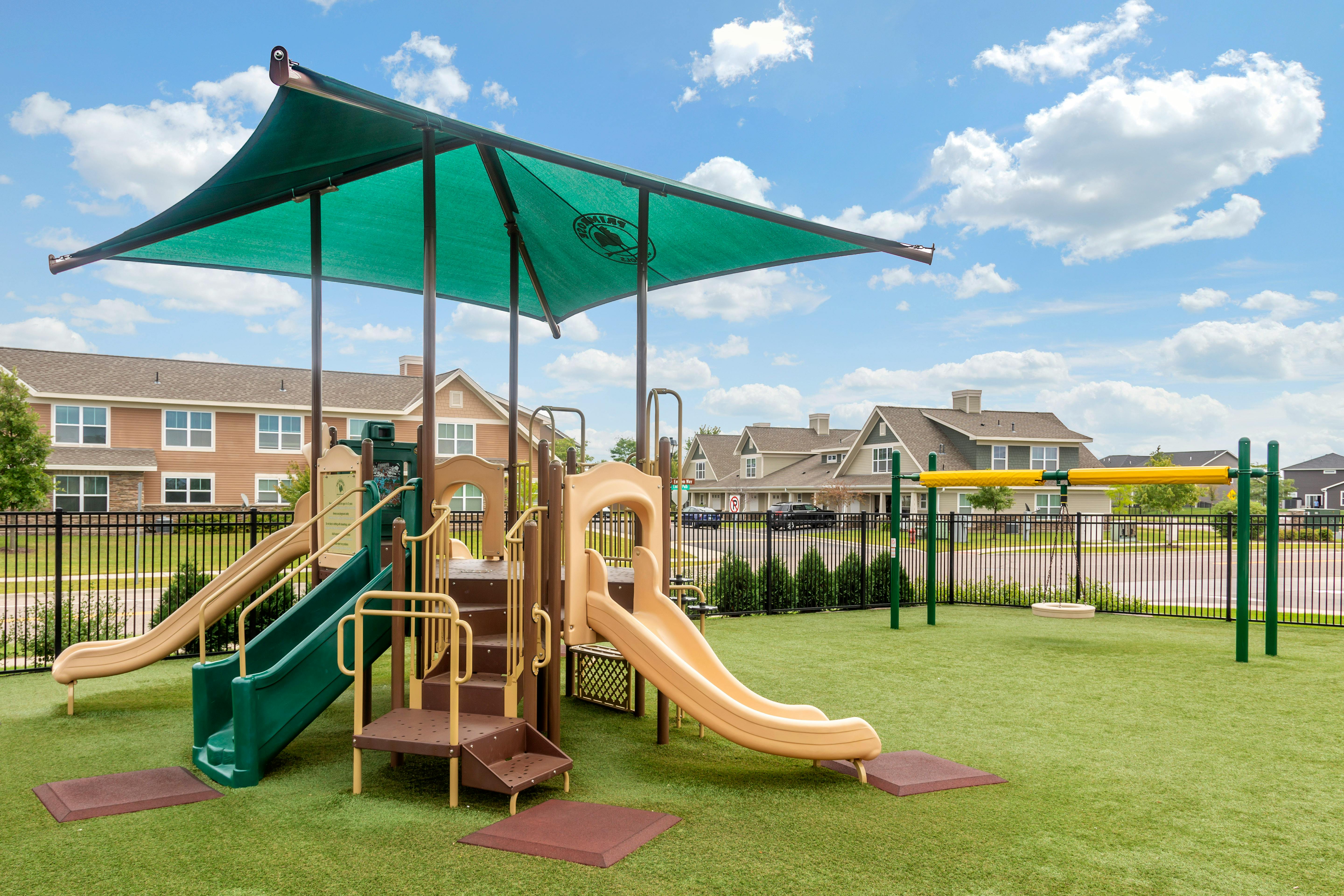 A playground with two slides and a swing, covered by a green shade