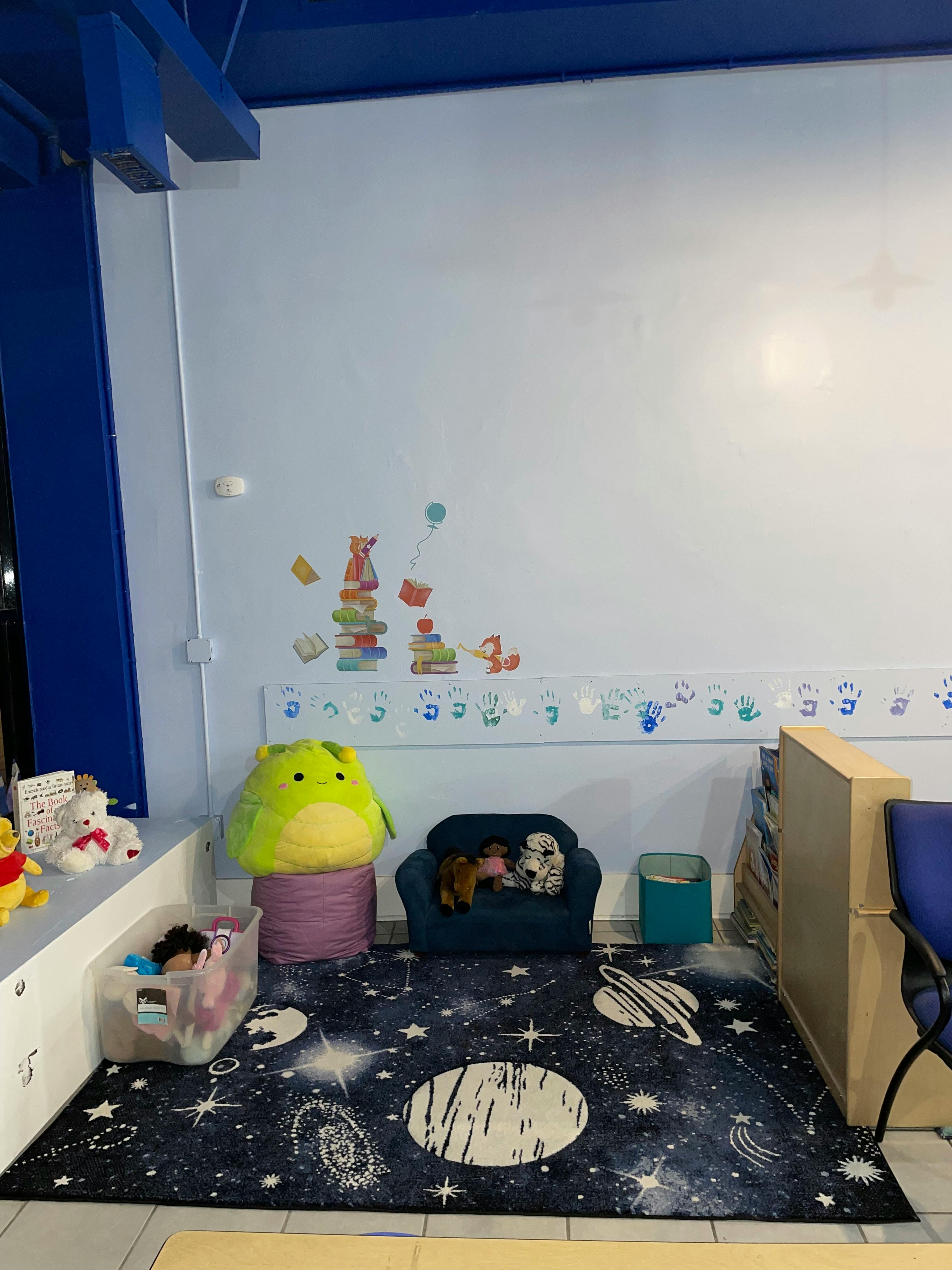 Children's play area with a space-themed rug, small couch, and stuffed animals