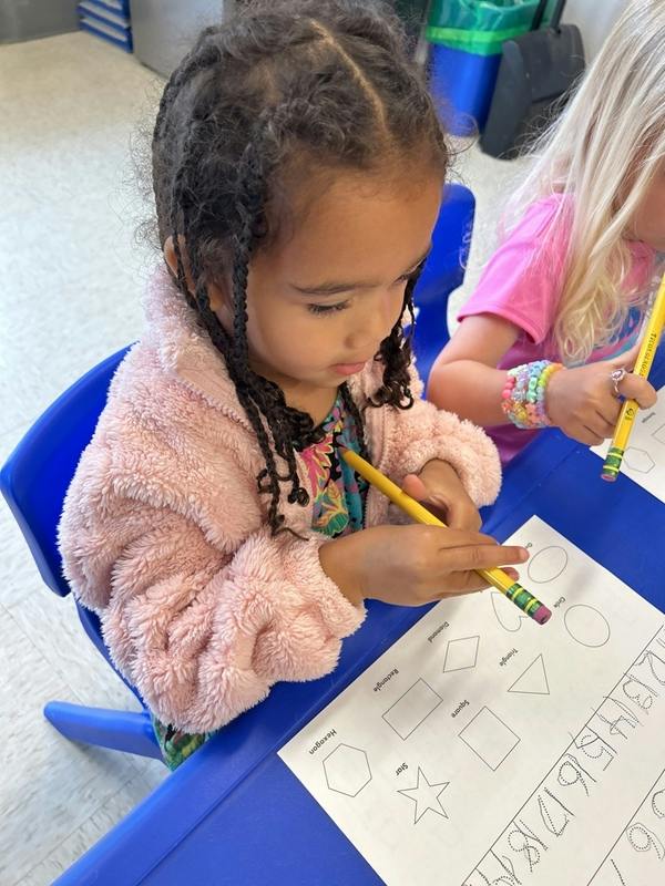 Child tracing shapes on a worksheet with a pencil