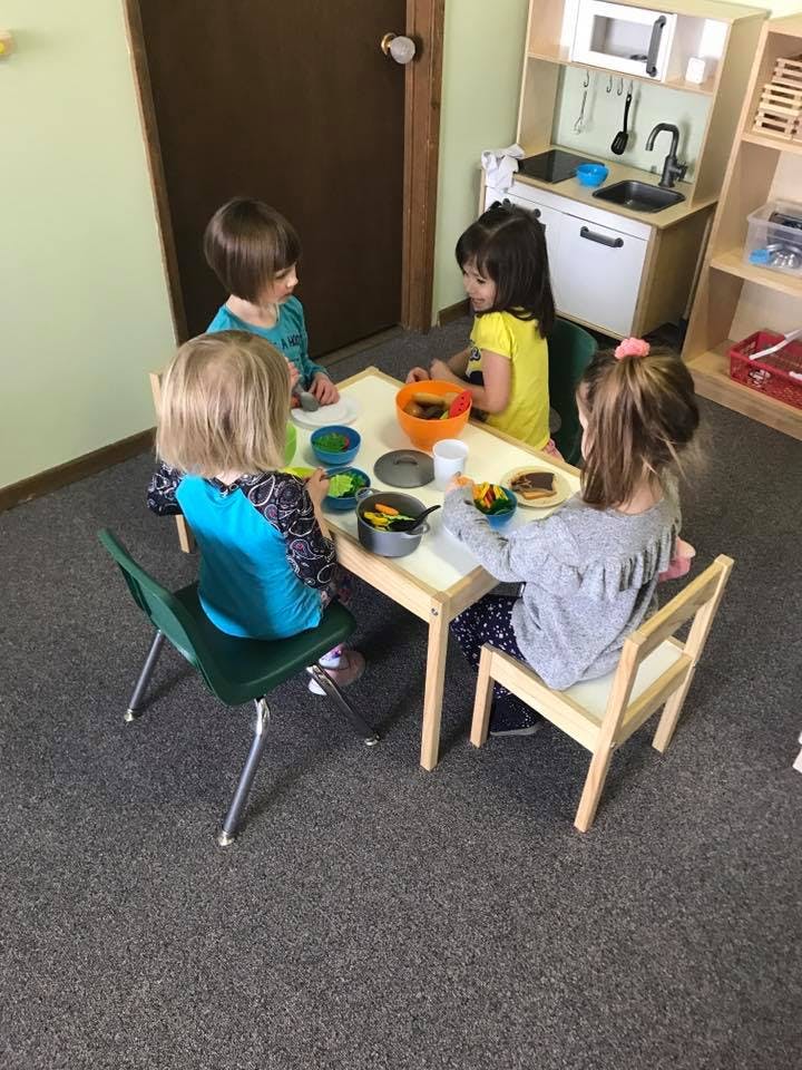 Four children sitting around a table with play food and craft items
