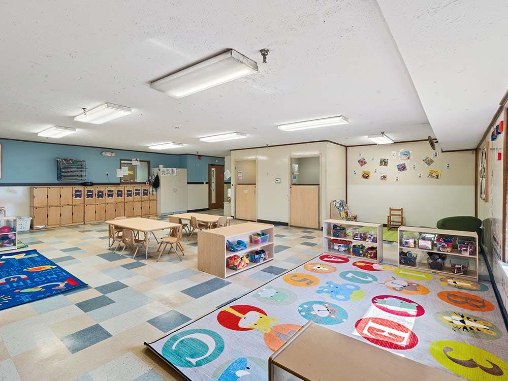 Empty classroom with small tables and chairs, storage cubbies, and colorful rugs
