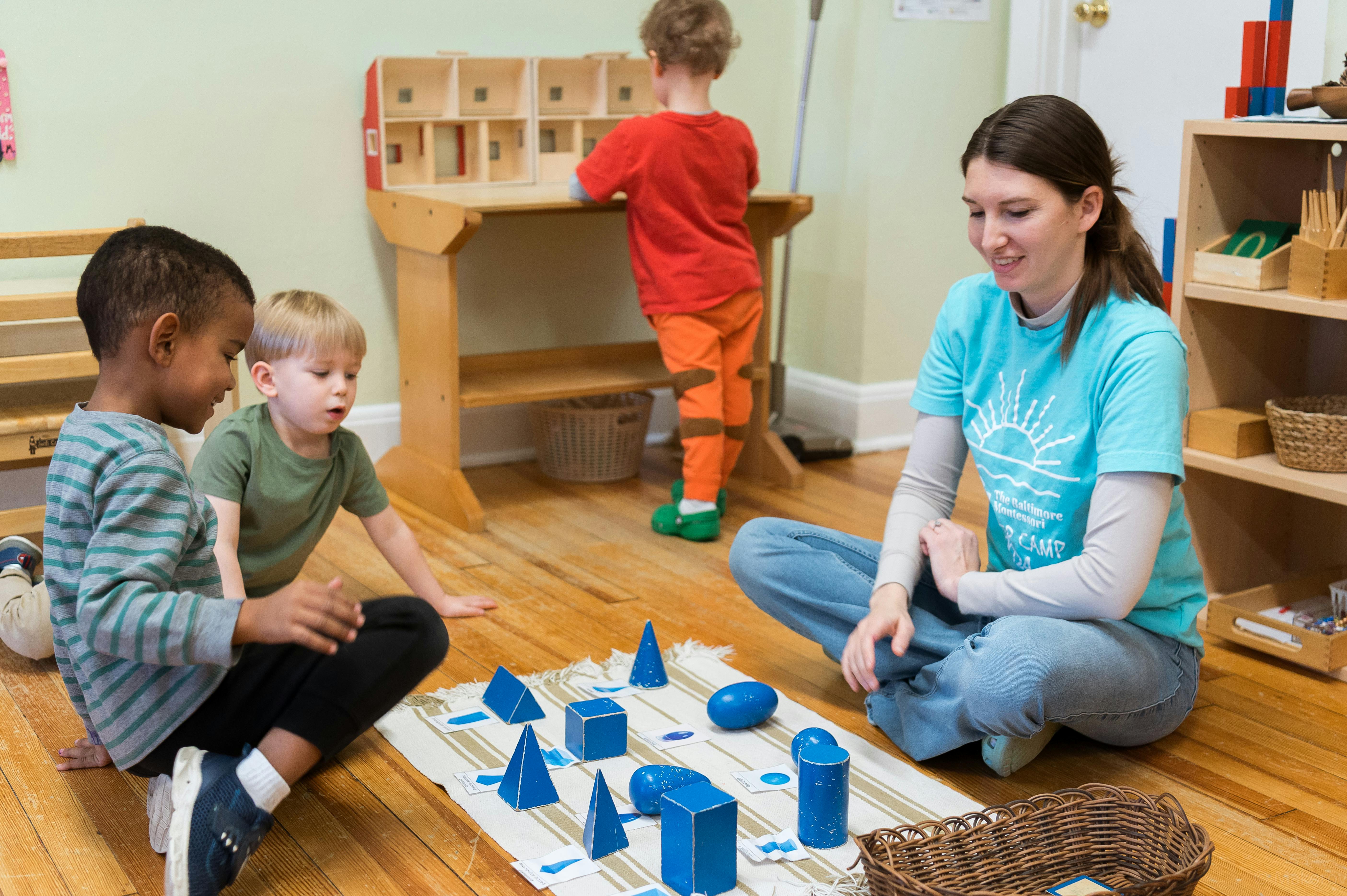 Adult and two children playing with blue geometric shapes on the floor
