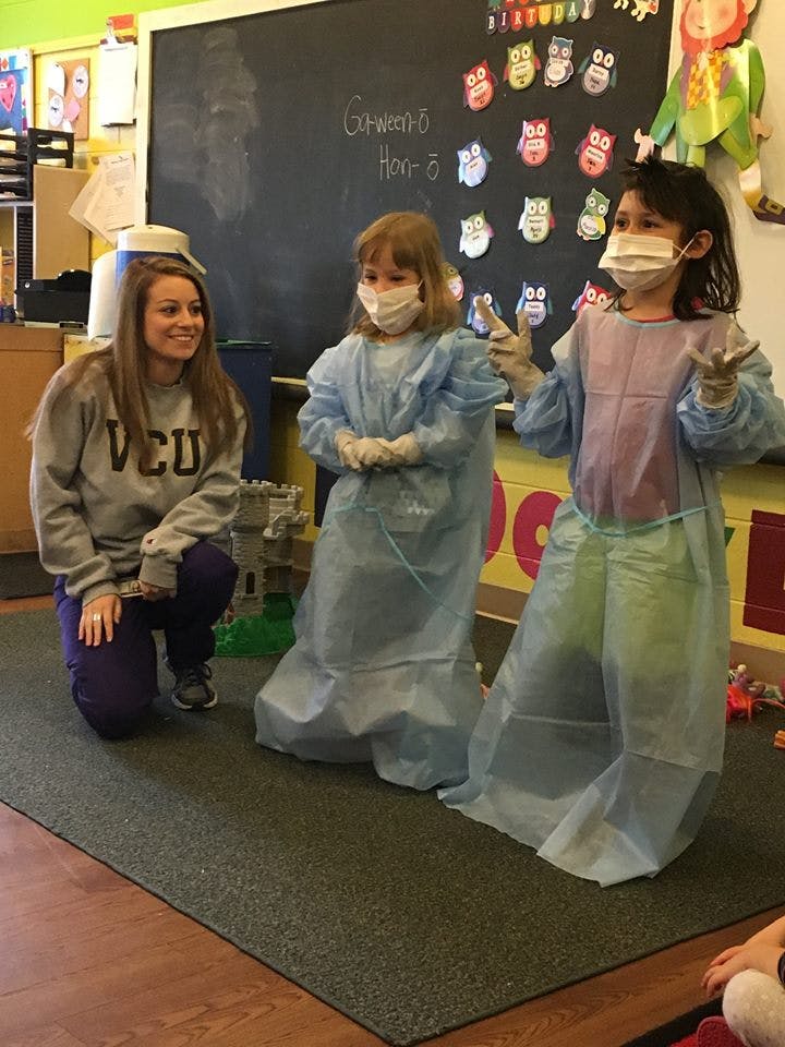 Adult and two children in masks and medical gowns in a classroom