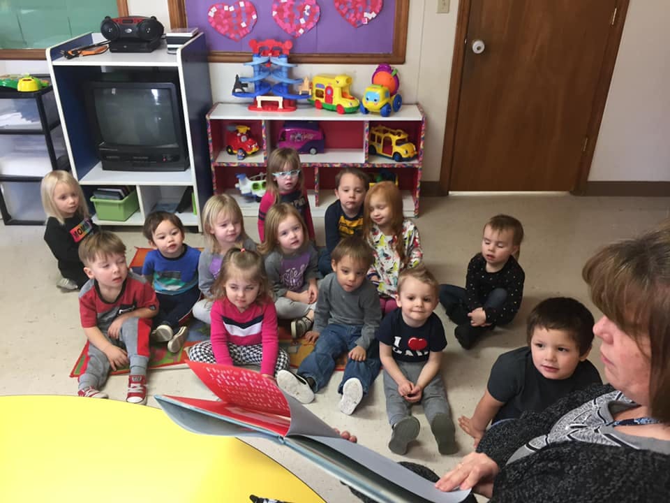 Adult reading a book to a group of children in a classroom
