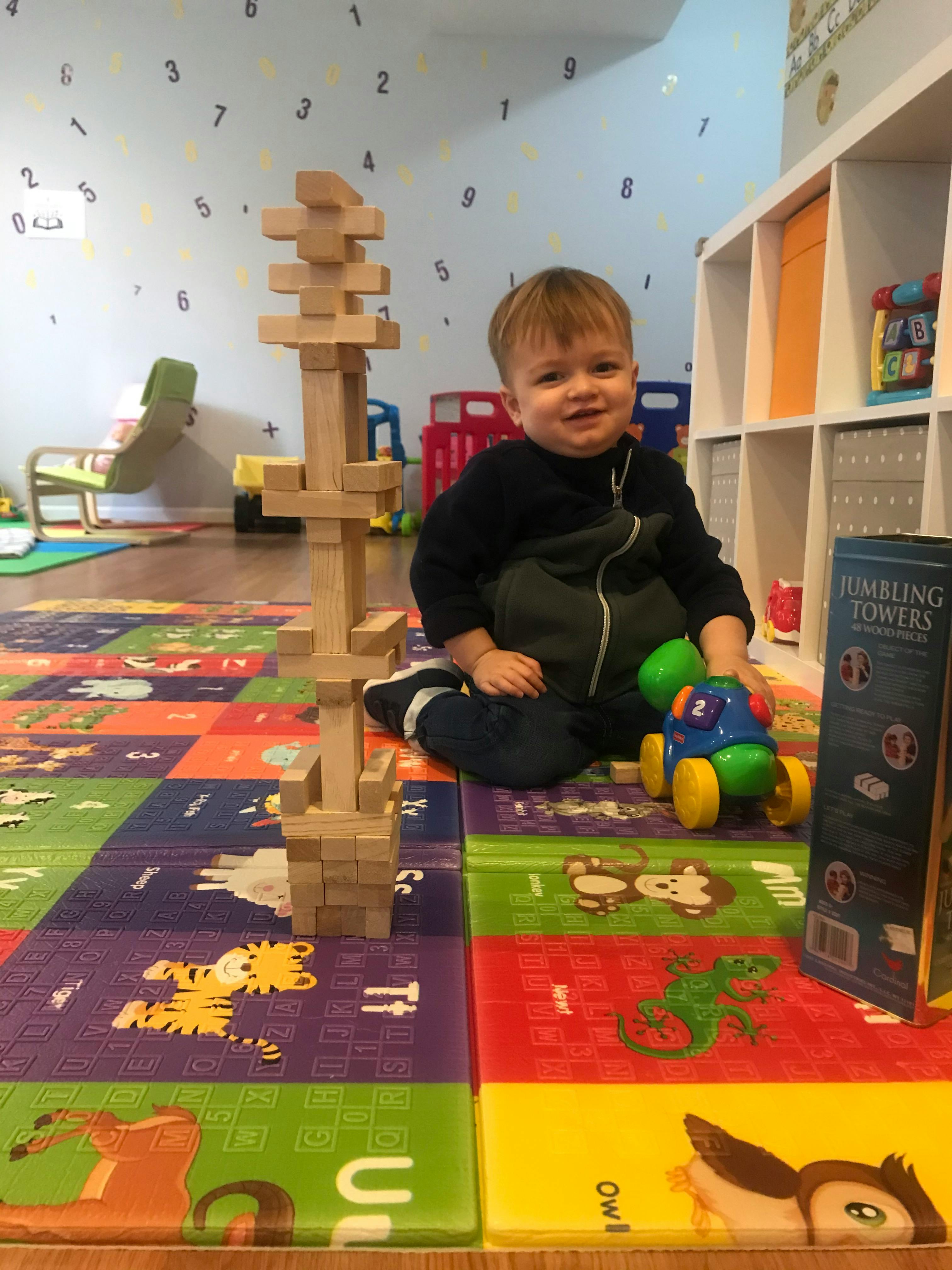 Child sitting on a playmat next to a tall wooden block tower