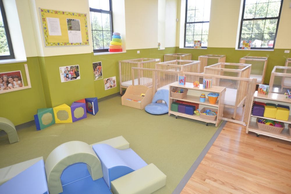 Nursery room with multiple cribs, soft play equipment, and windows