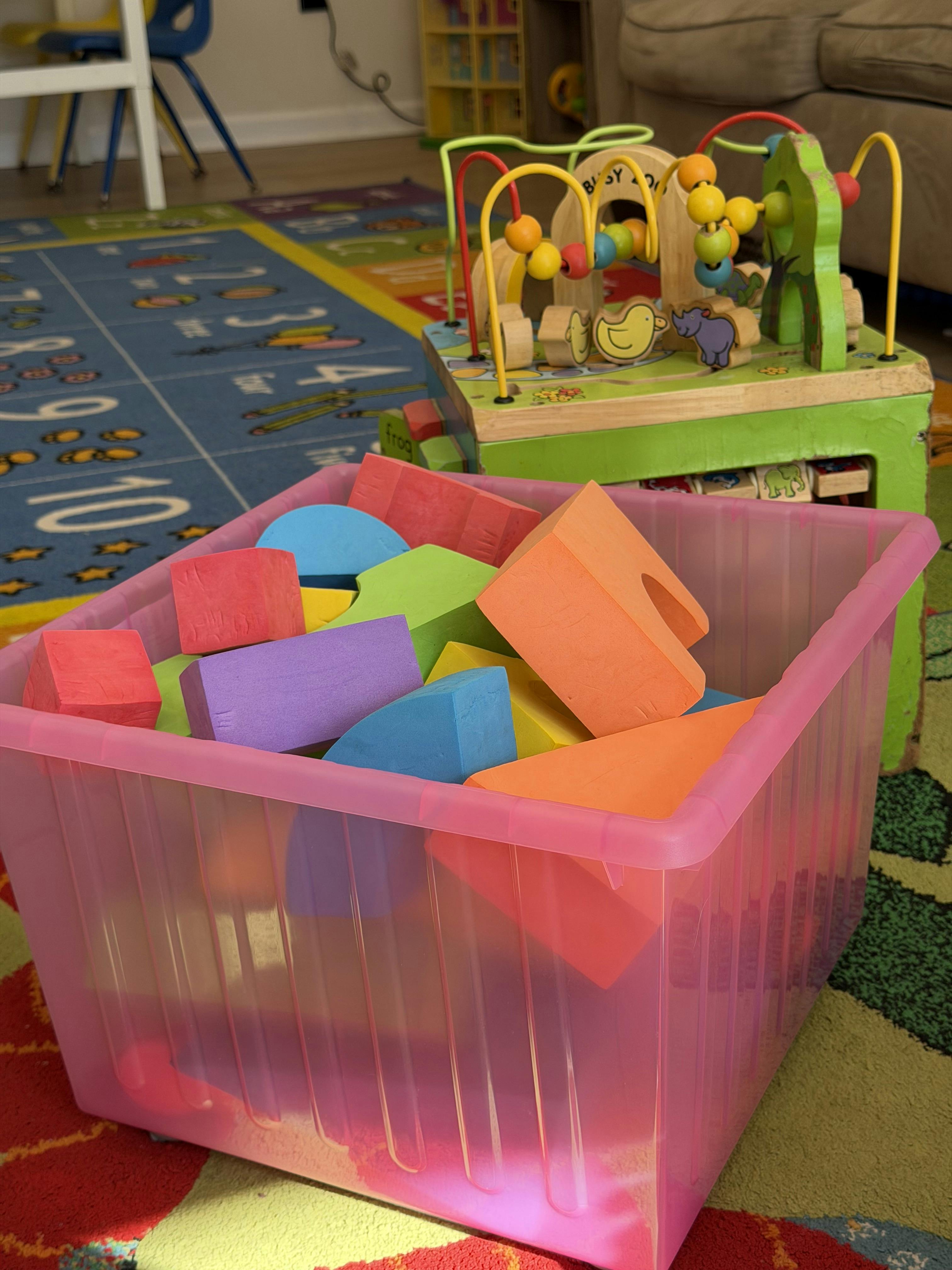 A pink bin filled with colorful foam blocks, next to a wooden activity cube