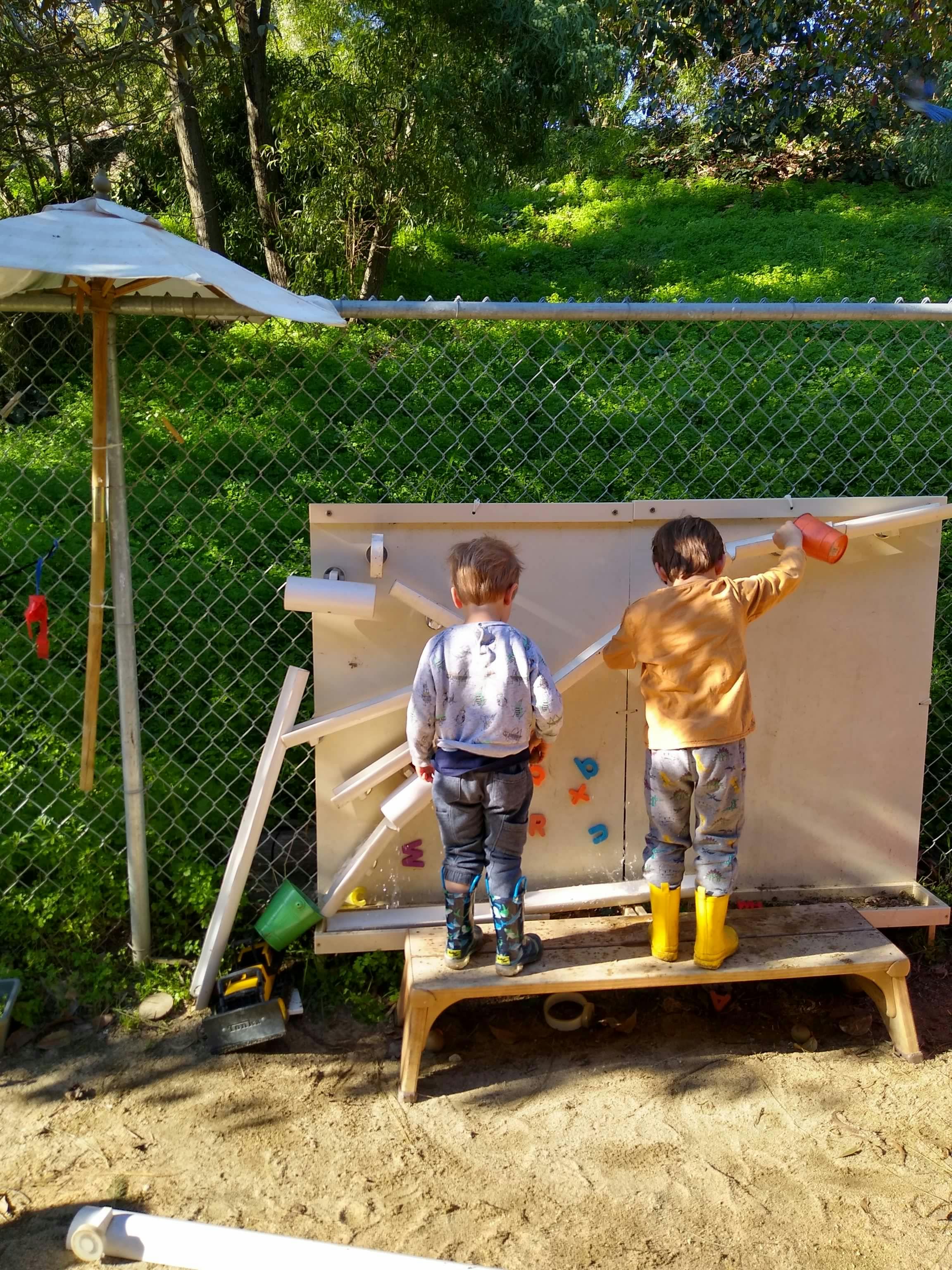 Two children playing at a water wall outdoors