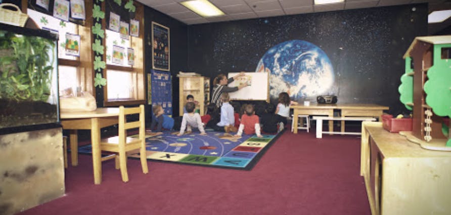Adult and children in a classroom with a large Earth mural