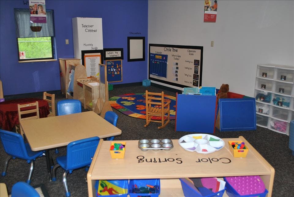 Classroom with child-sized tables, chairs, play kitchen, and teaching boards