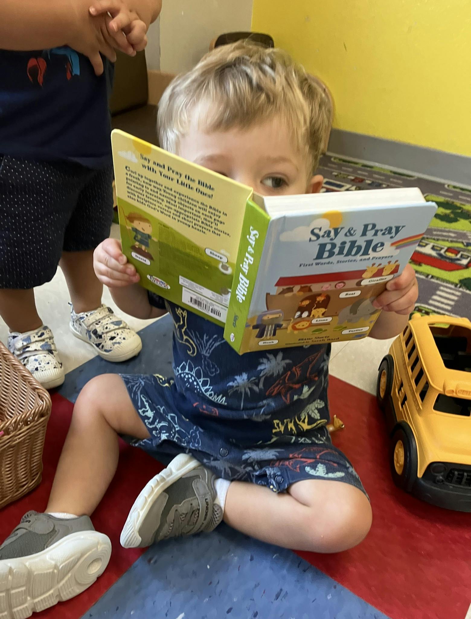 Child sitting on floor reading a book titled "Say & Pray Bible"