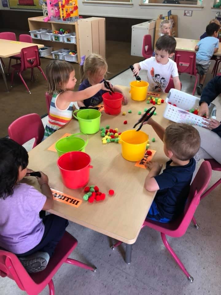 Children at a table using tongs to move pom-poms into buckets
