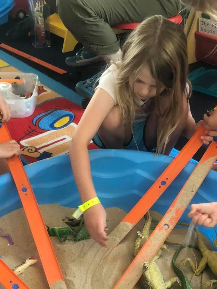 Child playing in a sand pit with toy lizards and orange tracks