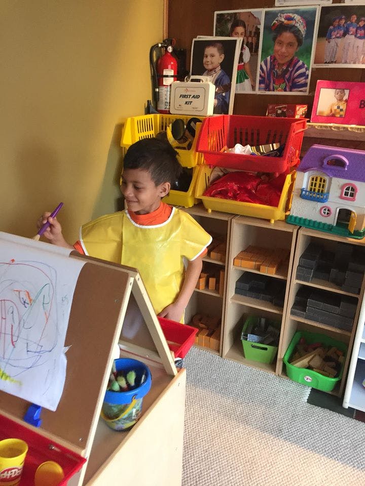 Child in a yellow smock painting at an easel