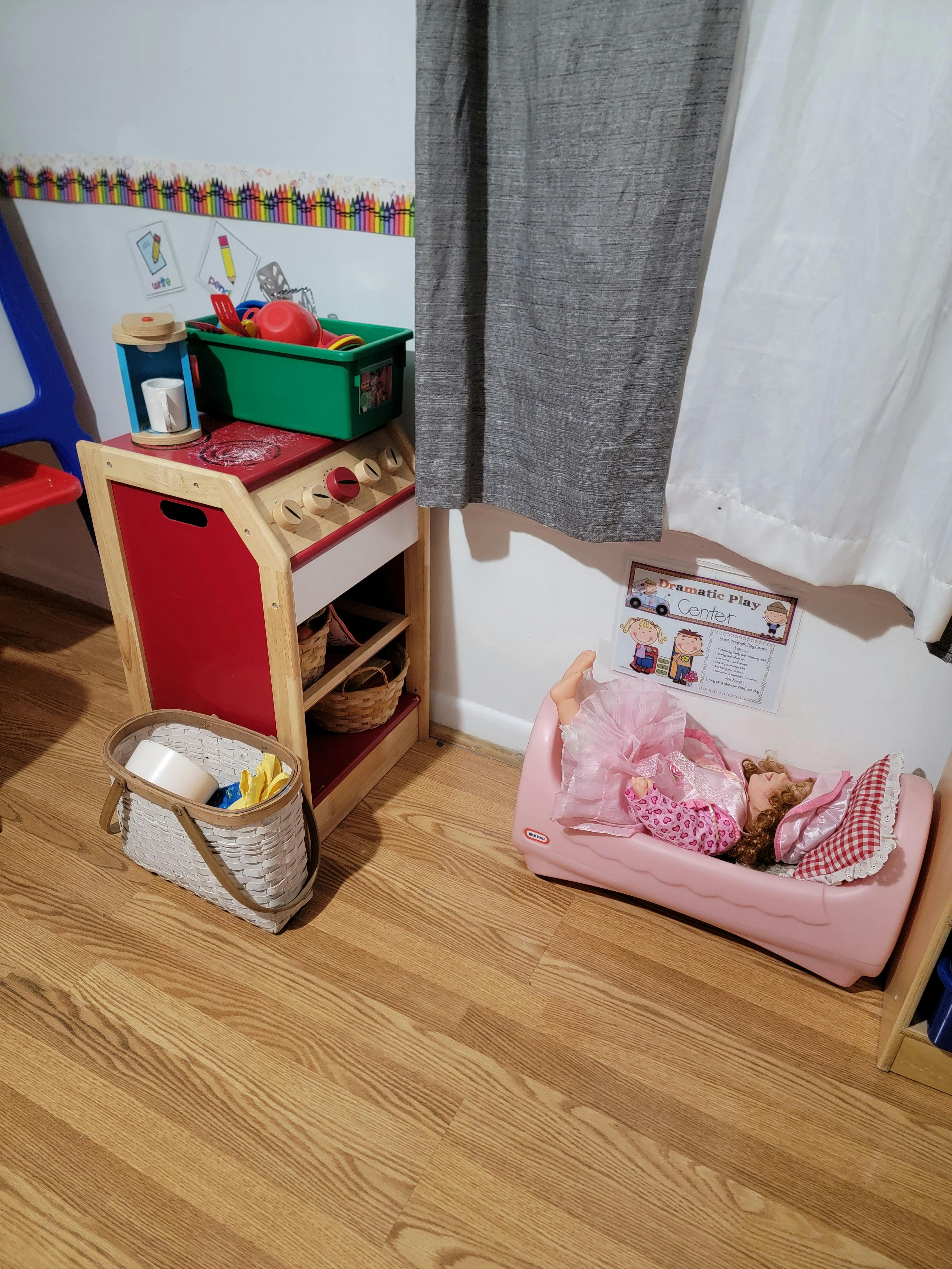 Doll in a pink bed next to a toy kitchen
