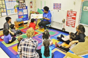 Adult reading a book to a group of children and adults in a classroom