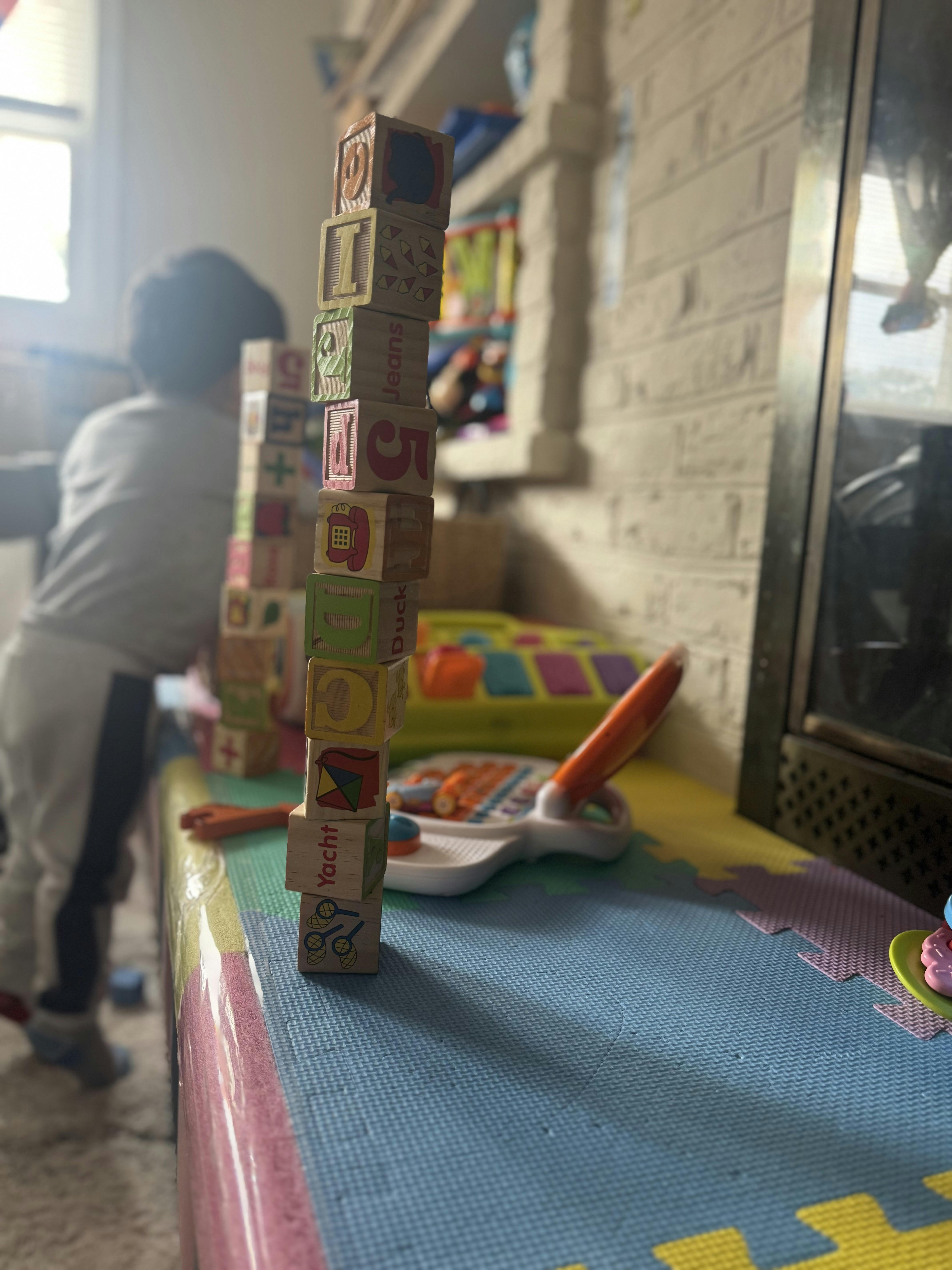 Child standing near a tall stack of alphabet blocks