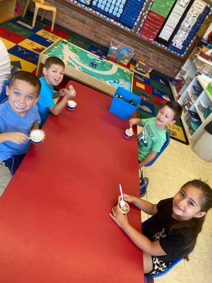 Four children sitting at a red table eating from cups with spoons