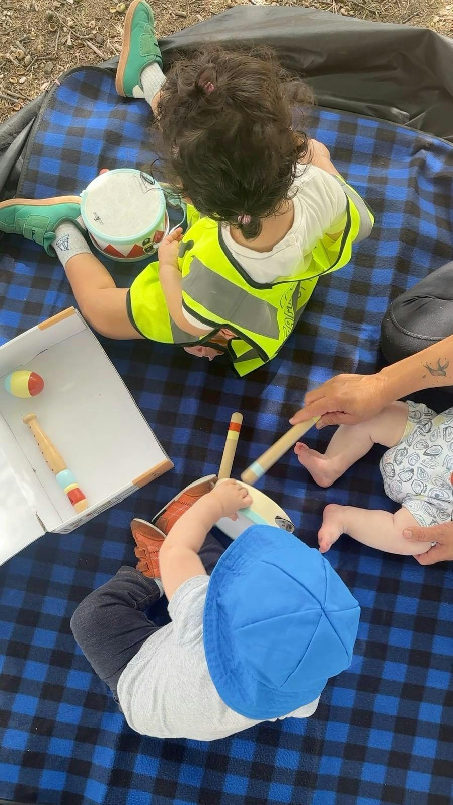 People playing with musical toy instruments on a plaid blanket