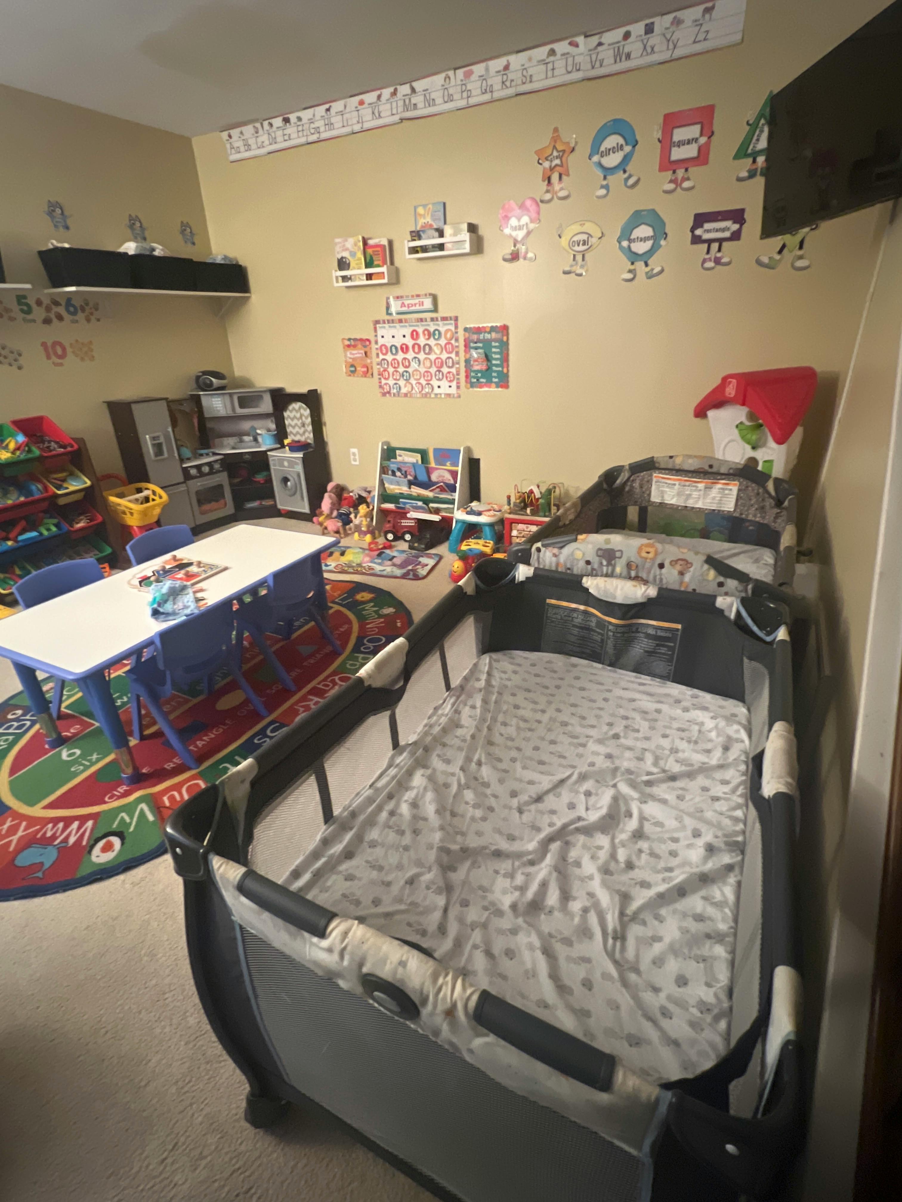 A child's playpen, a white table with blue chairs, and a play kitchen