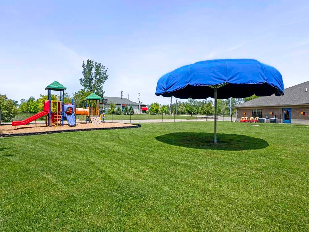 A playground with a blue umbrella on a grassy field