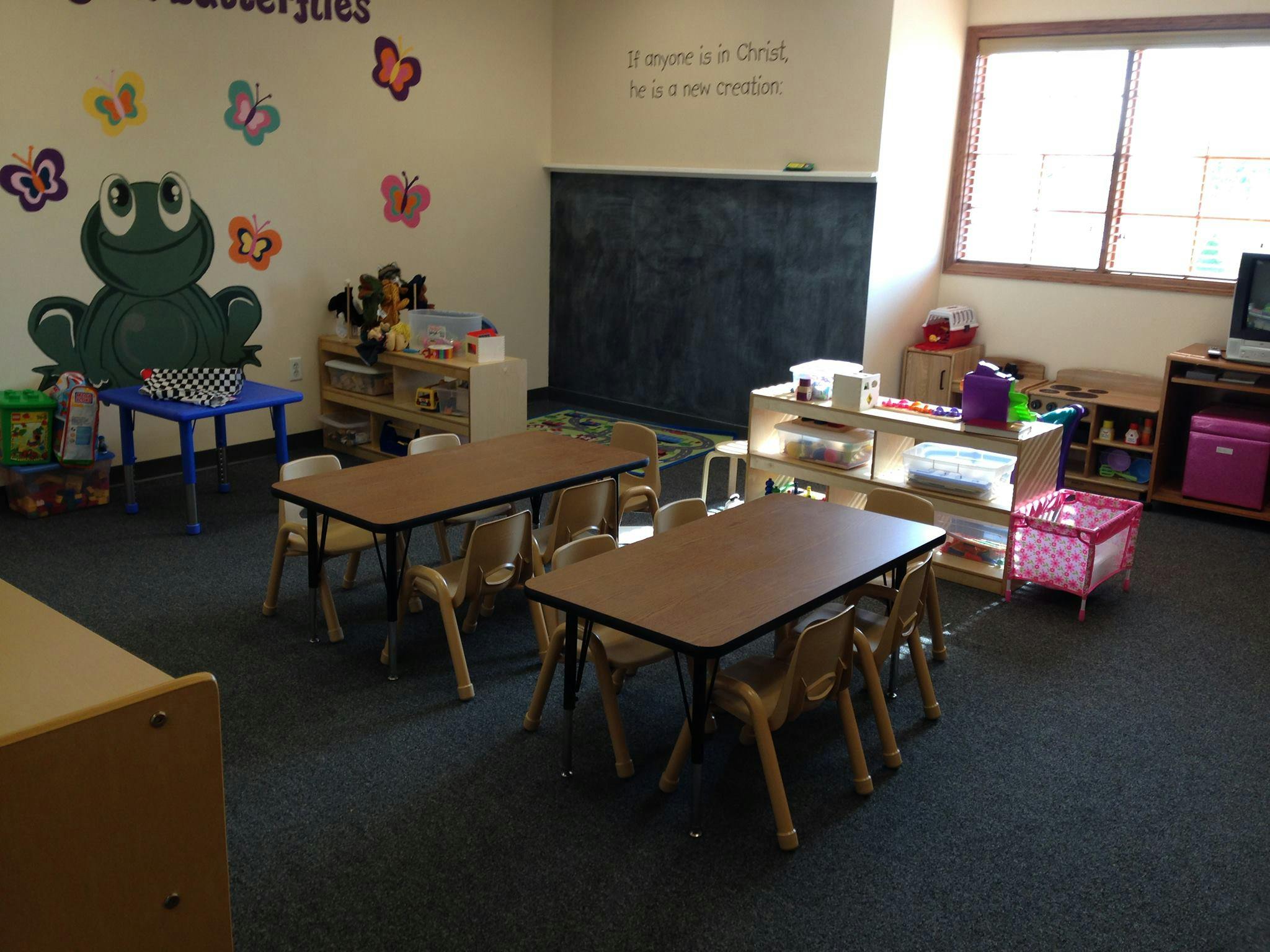 Classroom with small tables and chairs, chalkboard, and wall decorations