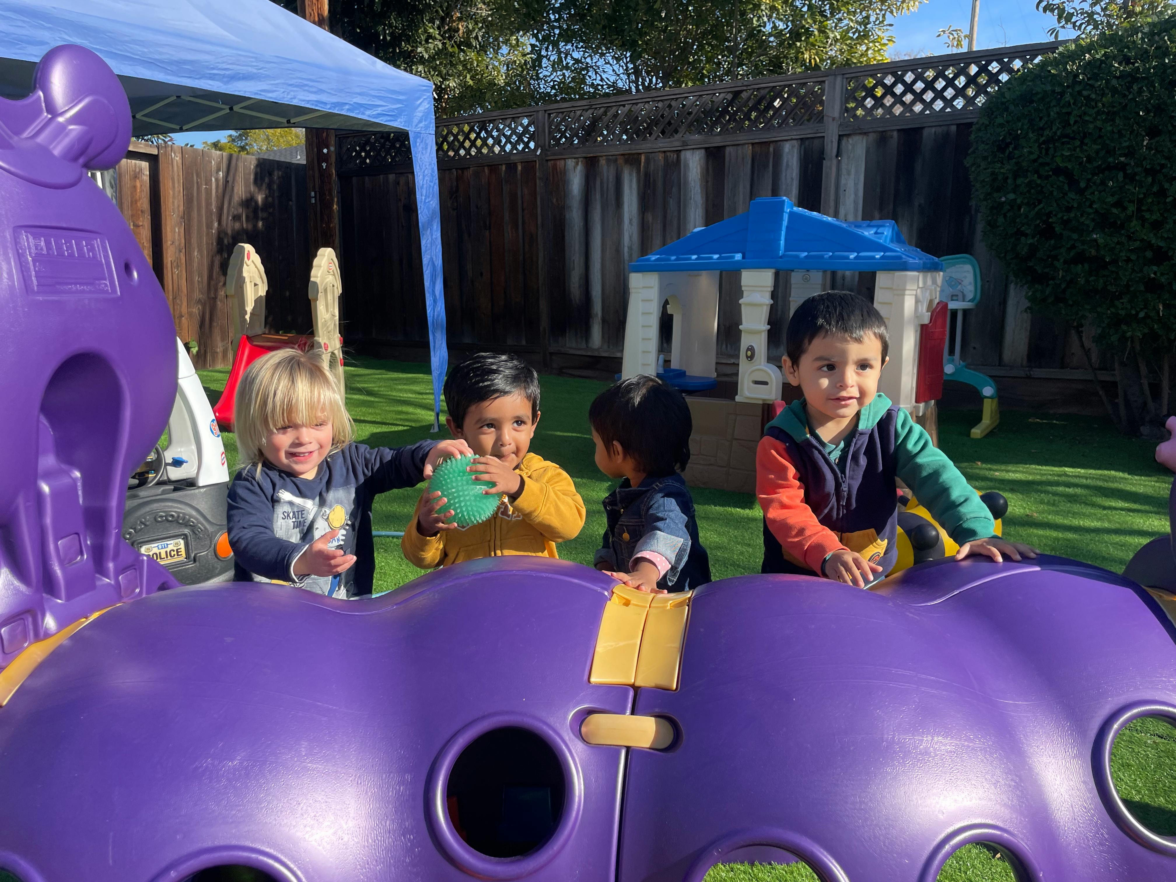 Four children playing on purple playground equipment outdoors