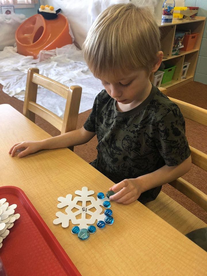 Child playing with a snowflake puzzle and blue glass beads at a table