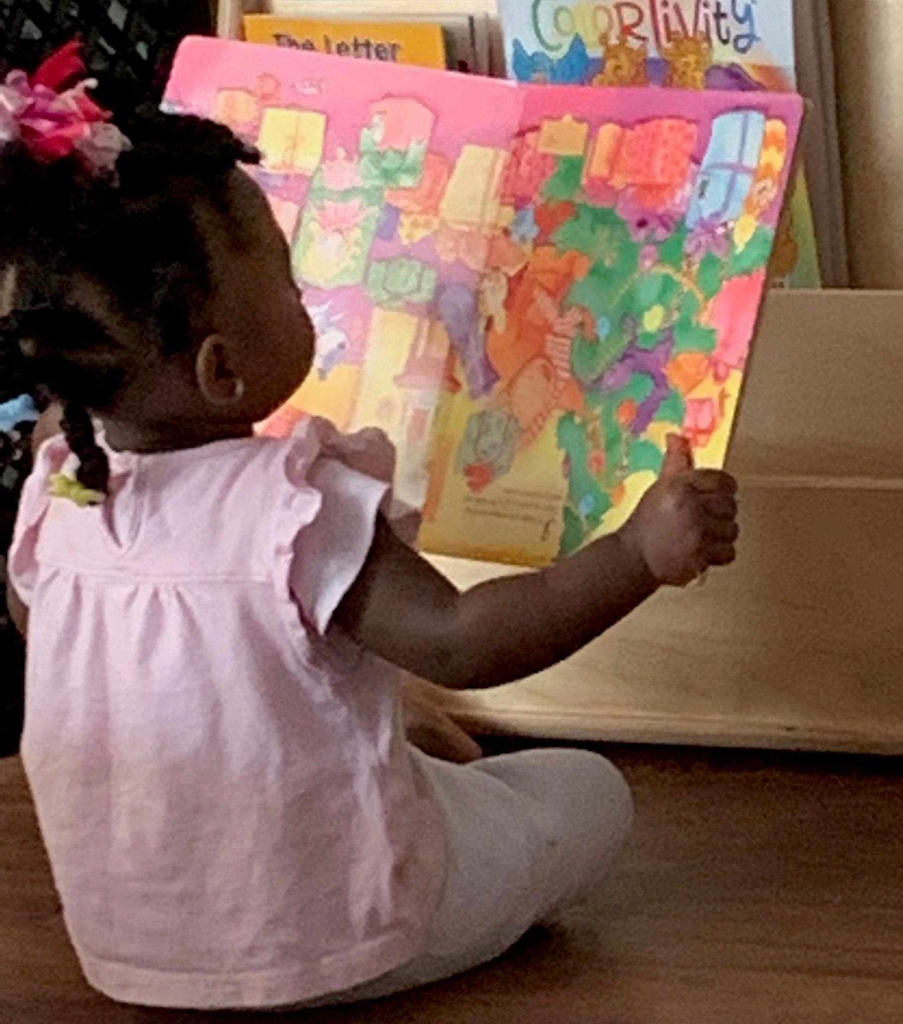 Child sitting on floor reading a colorful book