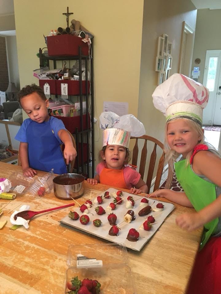 Three children making chocolate-covered fruit