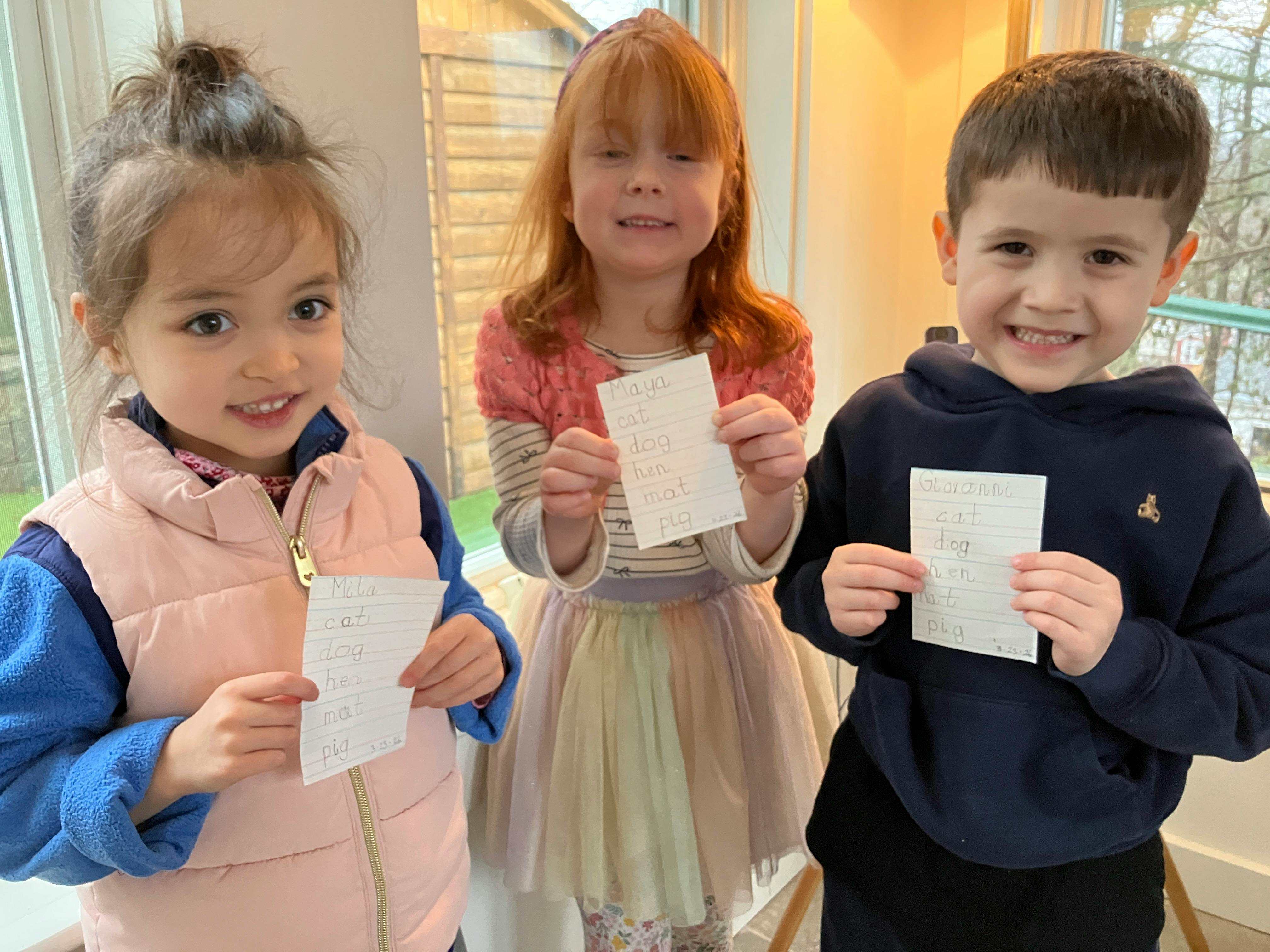 Three children holding up papers with handwritten words like "cat" and "dog"