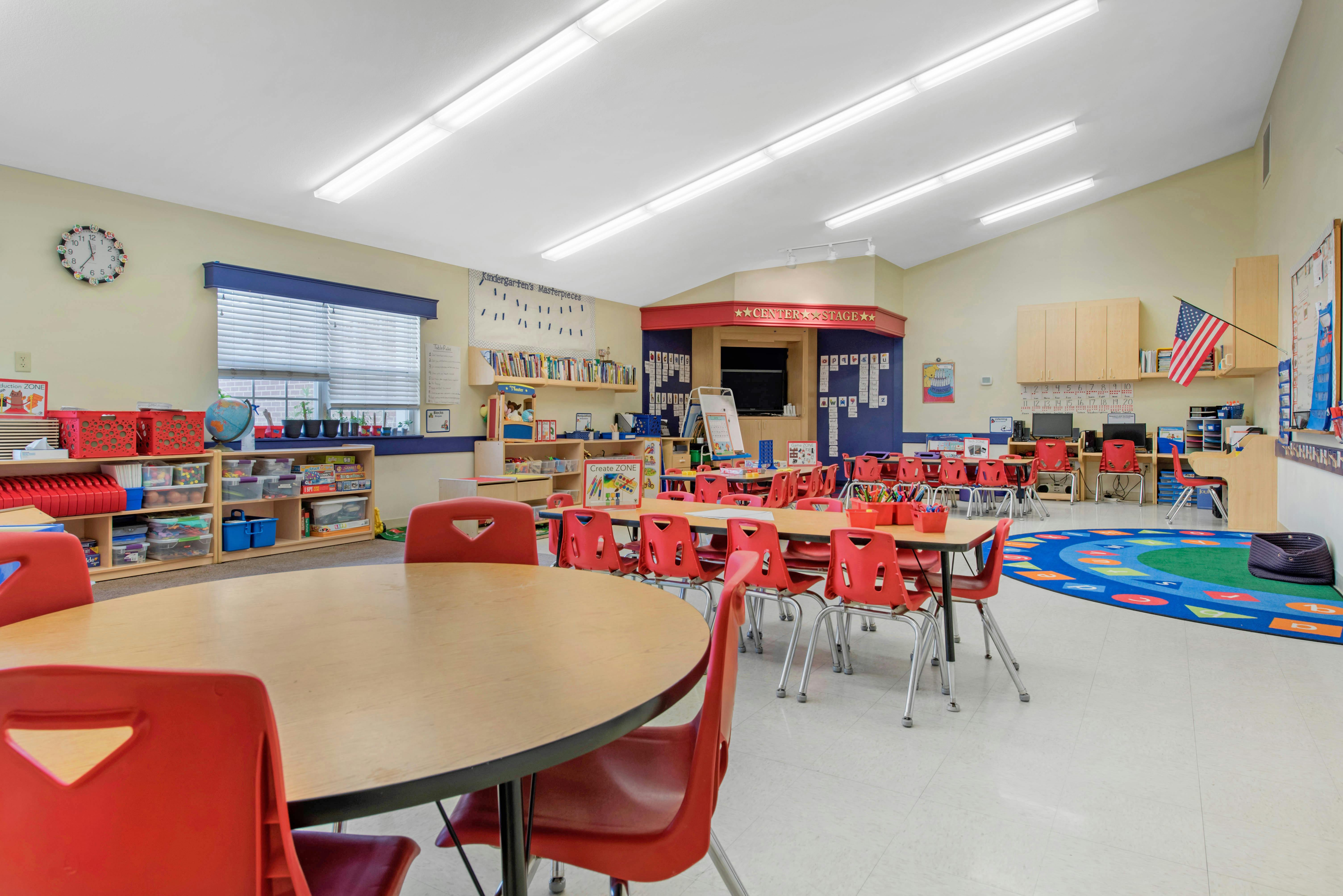 Empty kindergarten classroom with small tables and red chairs