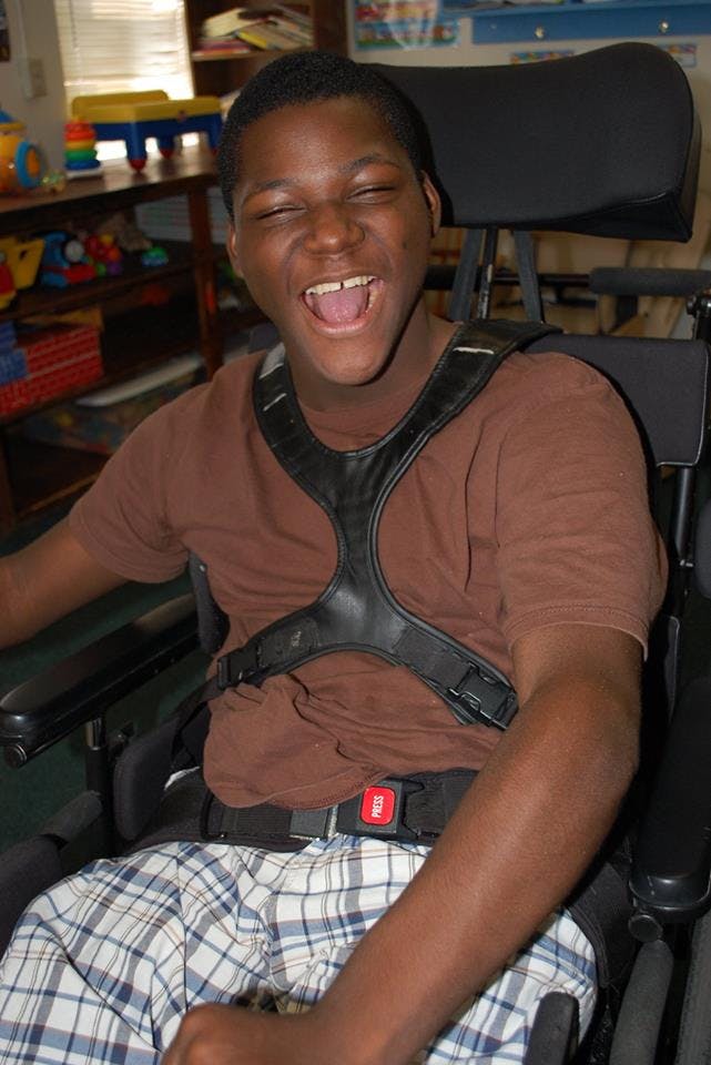 Person in a wheelchair with a harness, mouth open