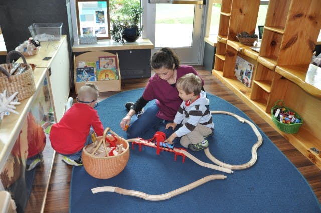 Adult and two children playing with a toy train set on a blue rug