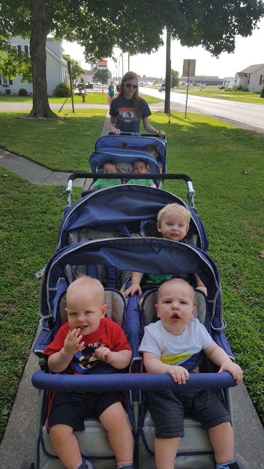 Person pushing multiple children in a long stroller train on a sidewalk