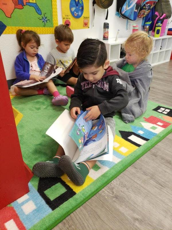 Four children sitting on a rug reading books in a classroom