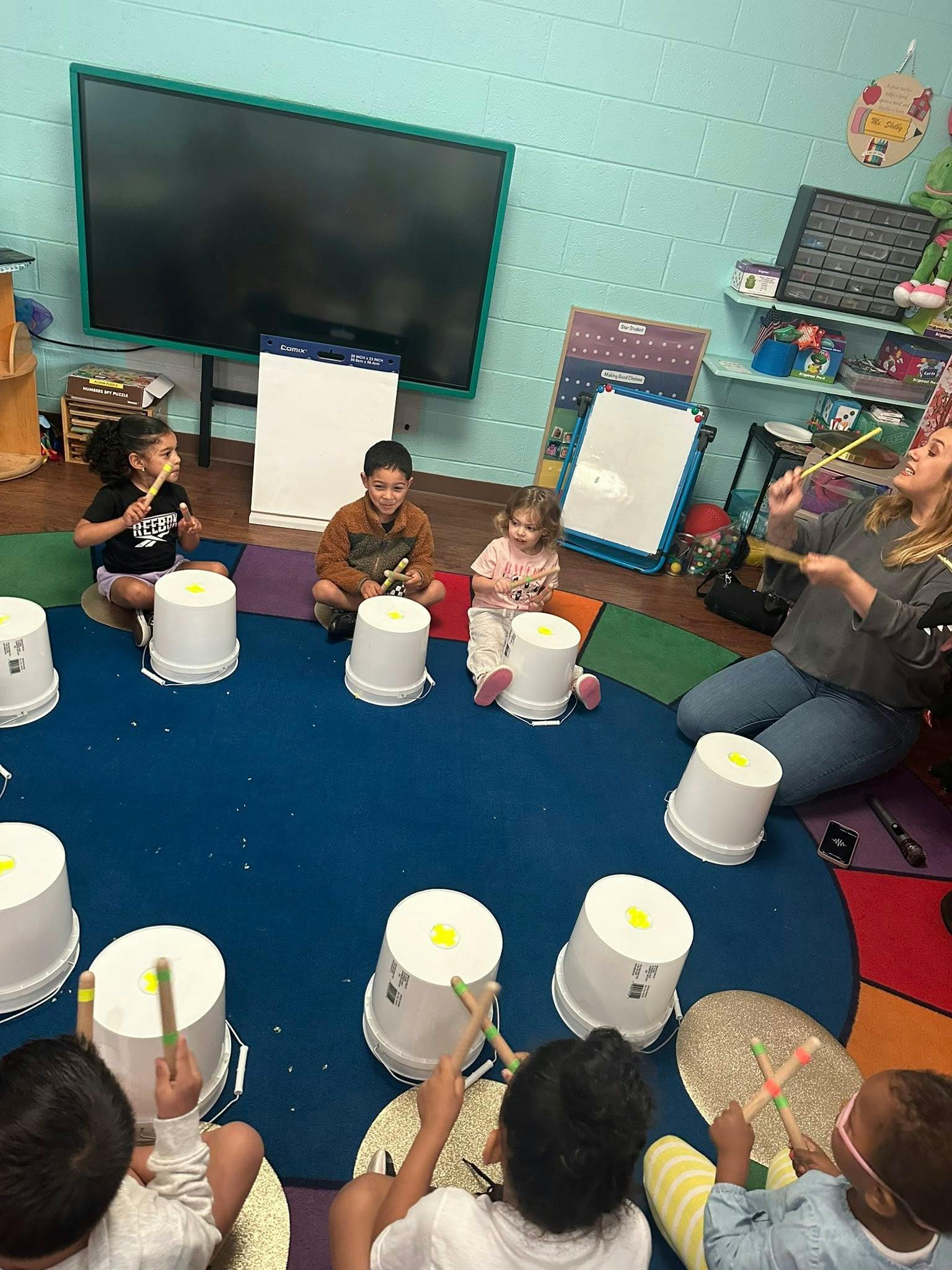 Adult and children playing drums made from buckets in a classroom