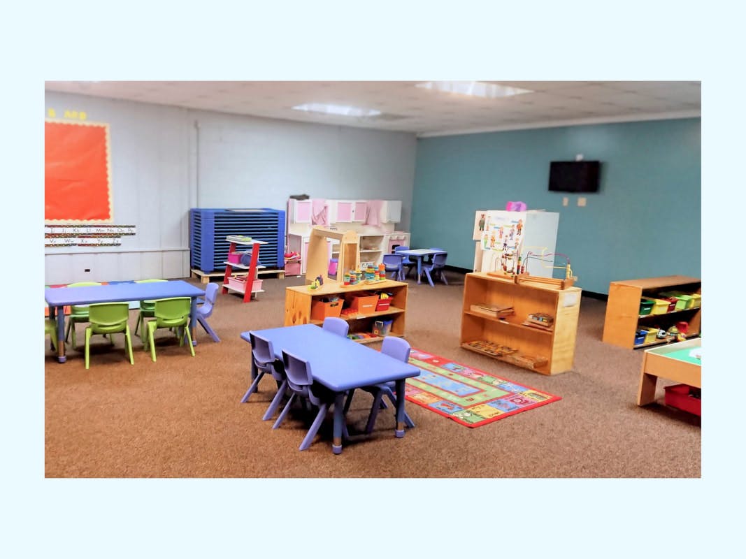 Classroom with small tables and chairs, shelves, and a colorful rug