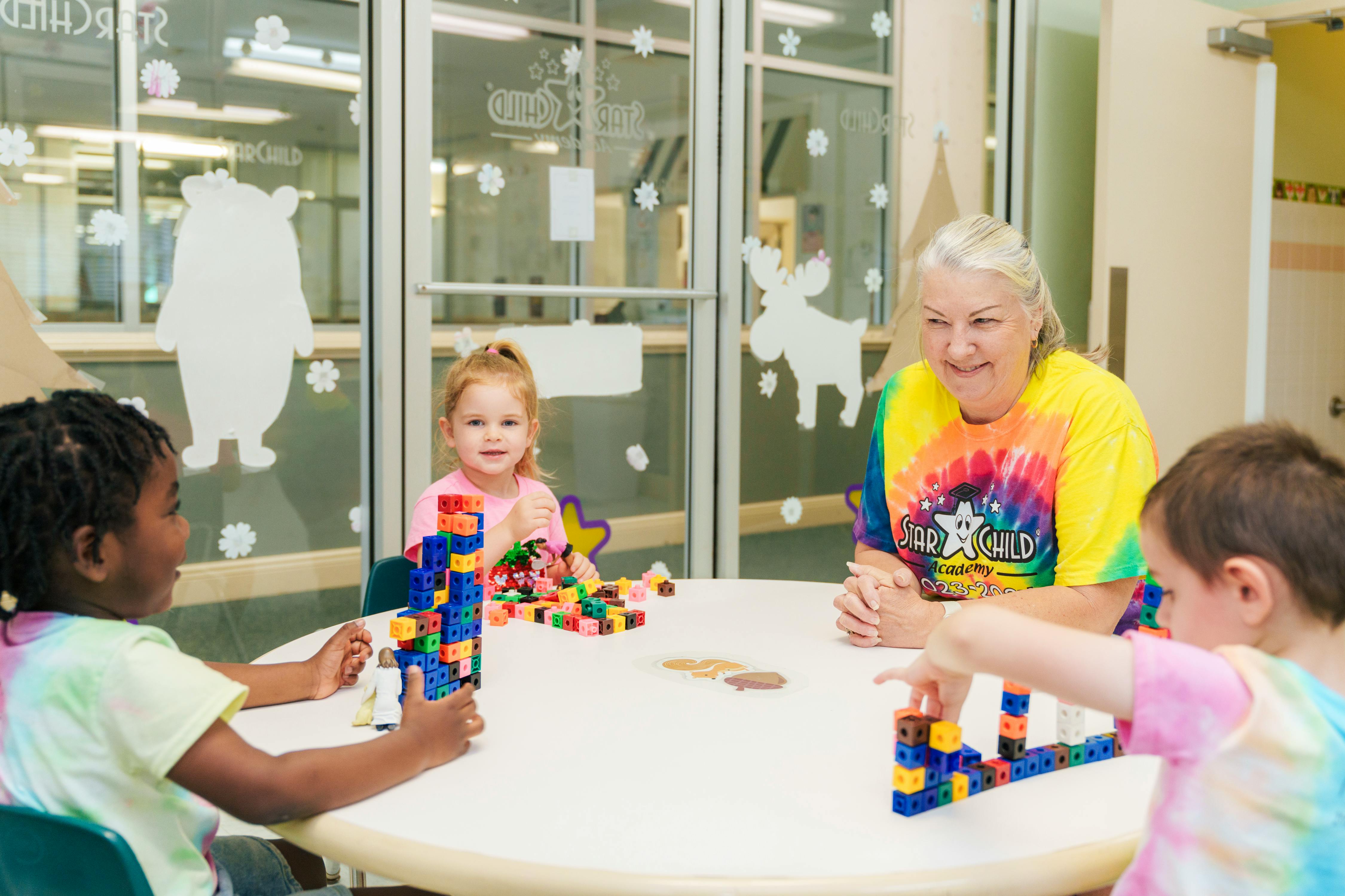 Adult and three children playing with building blocks at a table