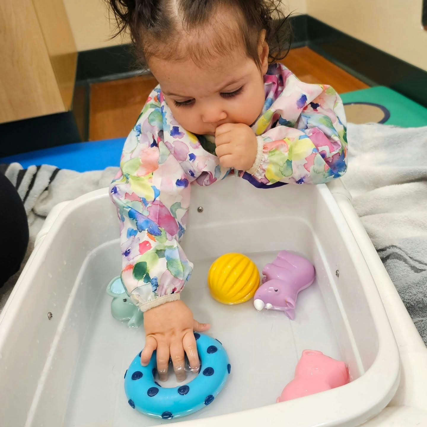 Child playing with floating plastic toys in a water basin