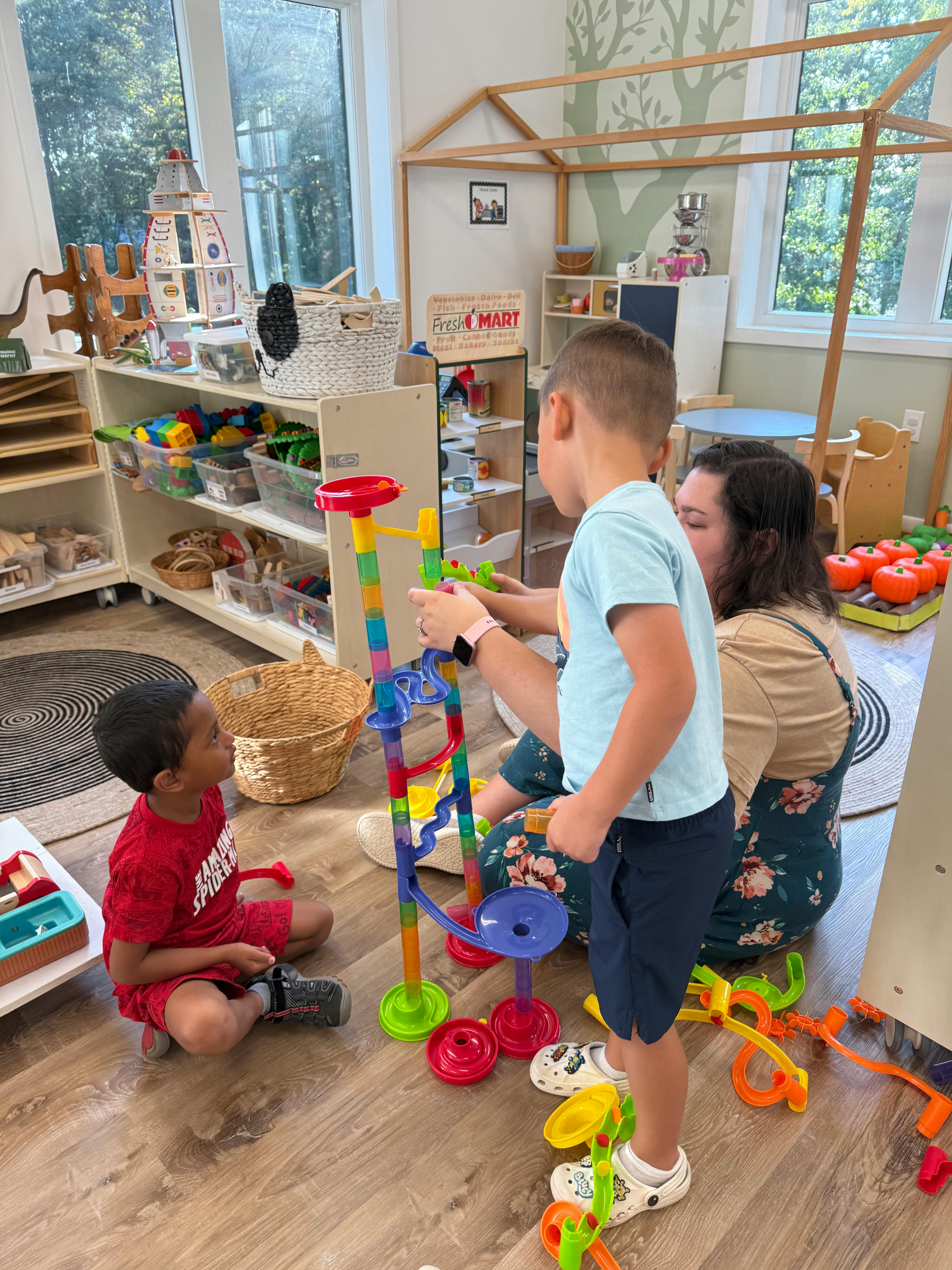 Two children and an adult playing with a colorful marble run toy