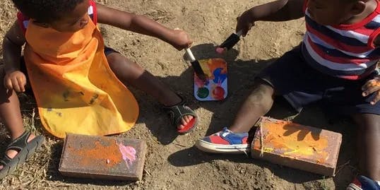 Two children painting bricks outdoors