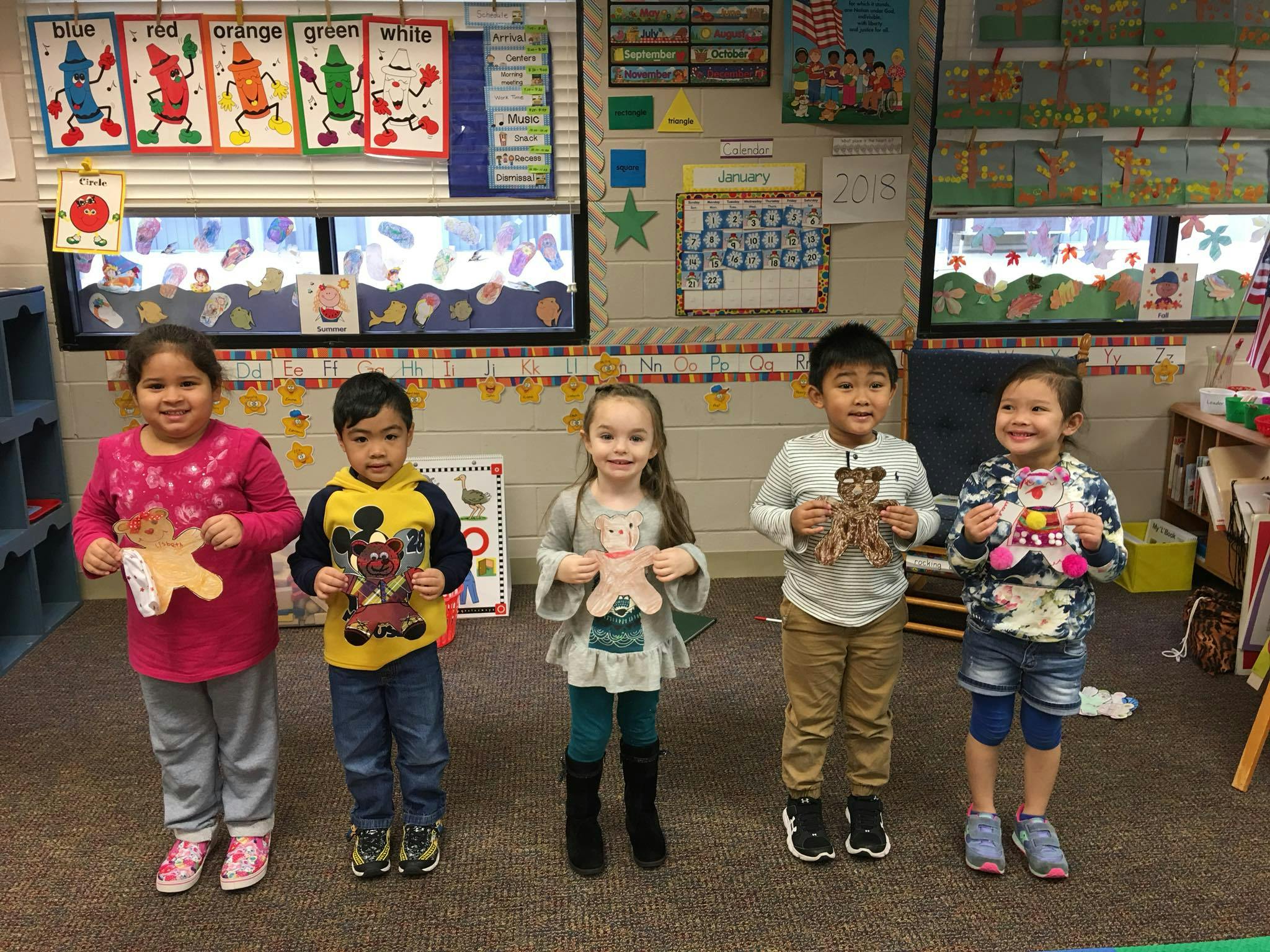 Five children holding paper cutouts in a classroom
