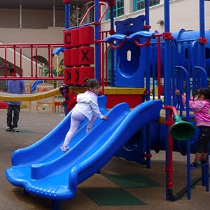 Child climbing up a blue slide on a playground