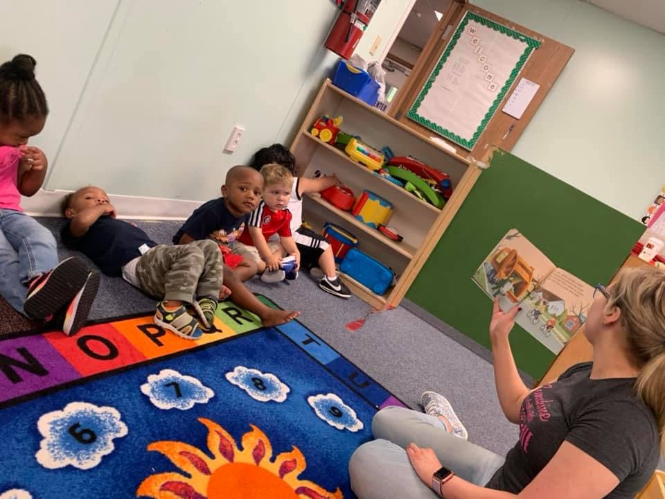 Adult reading a book to several children in a classroom